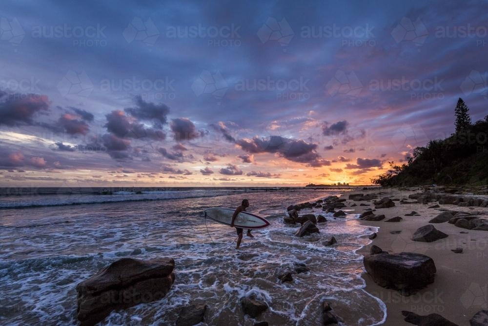 A surfer exiting the water at sunrise - Australian Stock Image