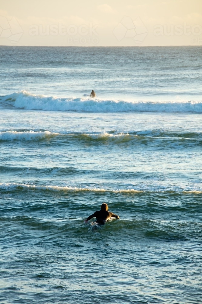 A surfer paddles out into the surf early in the morning at Cabarita. - Australian Stock Image