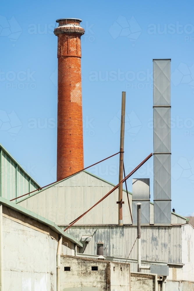 A tall brick chimney beside a large tin factory - Australian Stock Image
