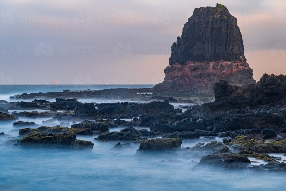 A tall rock formation jutting above a rocky coastline - Australian Stock Image