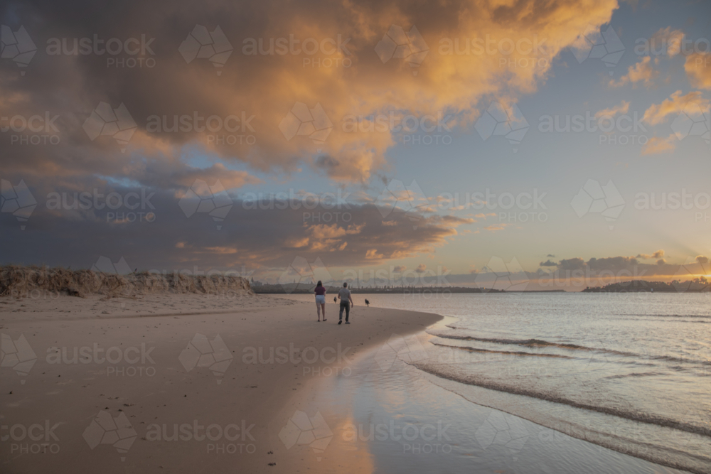 A teenage boy and girl walking on a beach at sunrise under a cloudy sky - Australian Stock Image