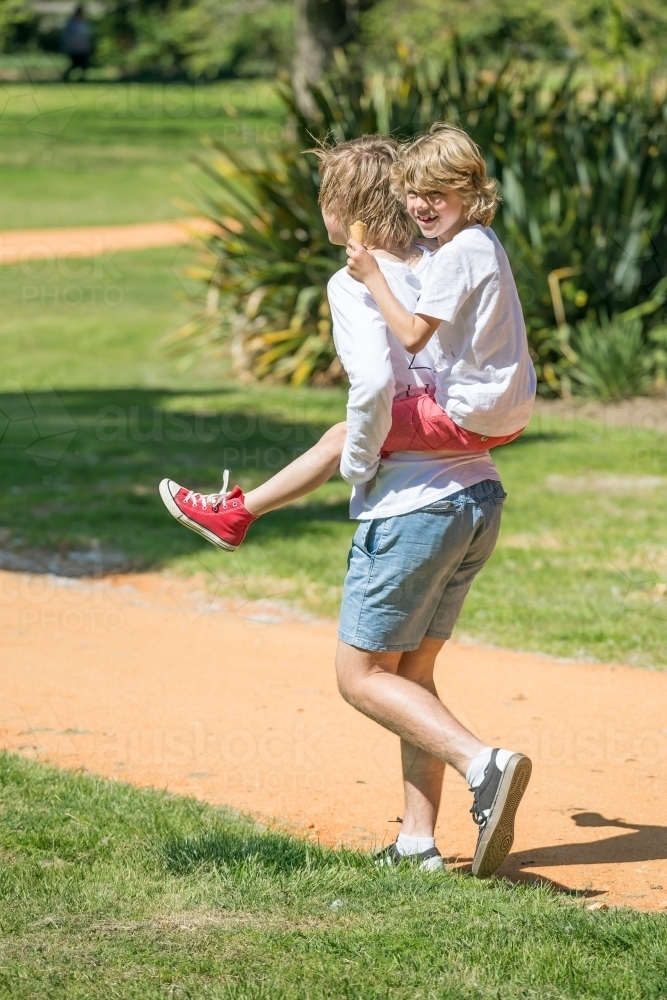 A teenage boy piggy backs his little brother - Australian Stock Image