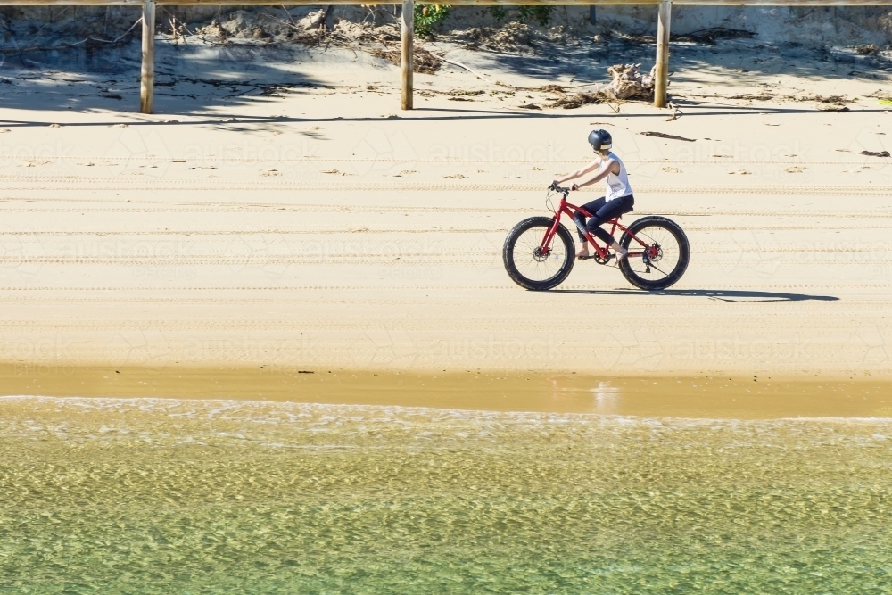 Image of A teenage girl riding a sand bike along a beach - Austockphoto