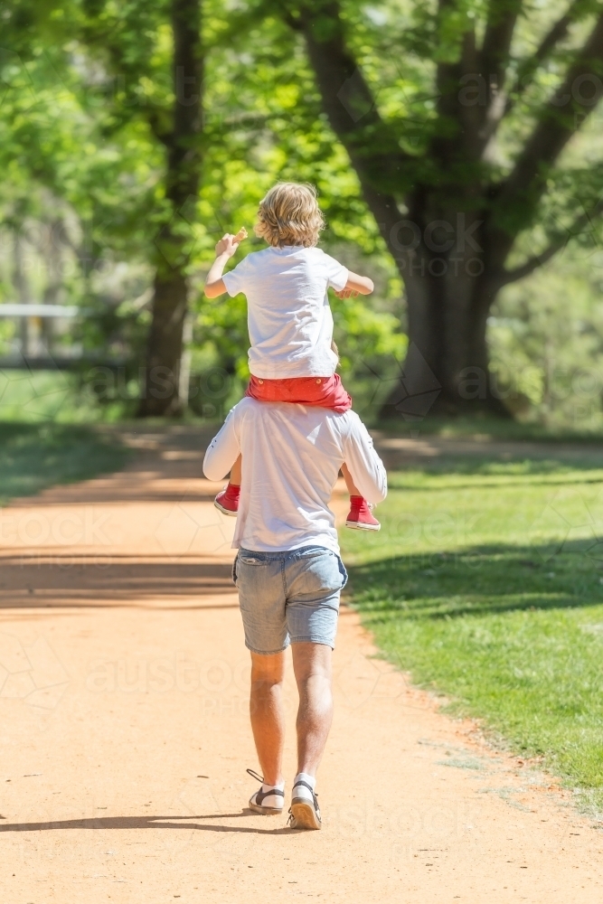 A teenager walking in a park with his little brother on his shoulders - Australian Stock Image