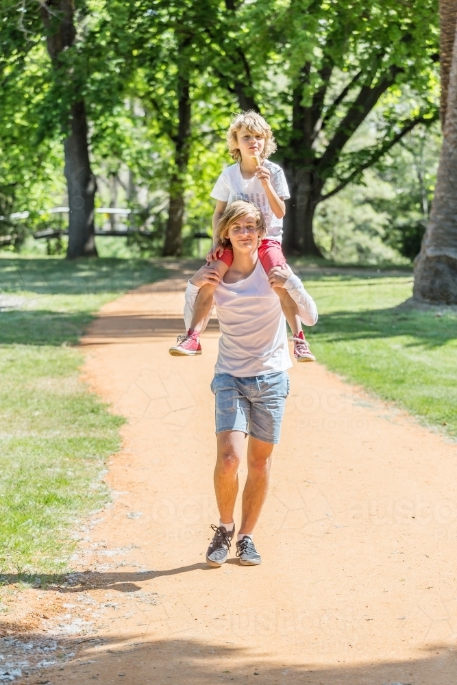A teenager walking the park with his little brother on his shoulders - Australian Stock Image