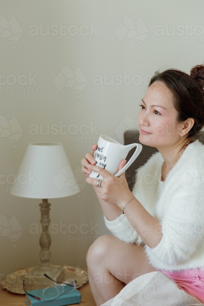 A thoughtful woman drinking tea on her bed - Australian Stock Image