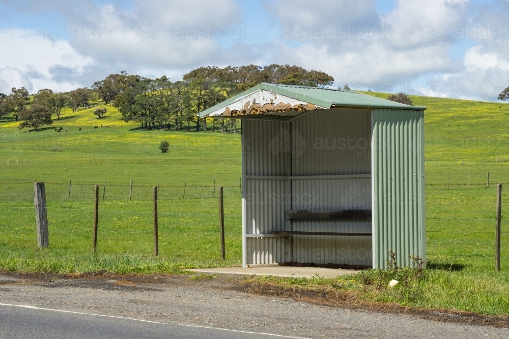 A tin bus shelter on a country road below green hills - Australian Stock Image