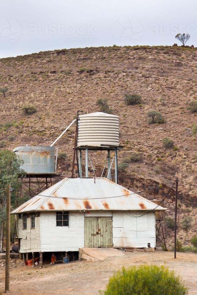 A tin shed and rainwater tanks at the base of a hill in the outback - Australian Stock Image