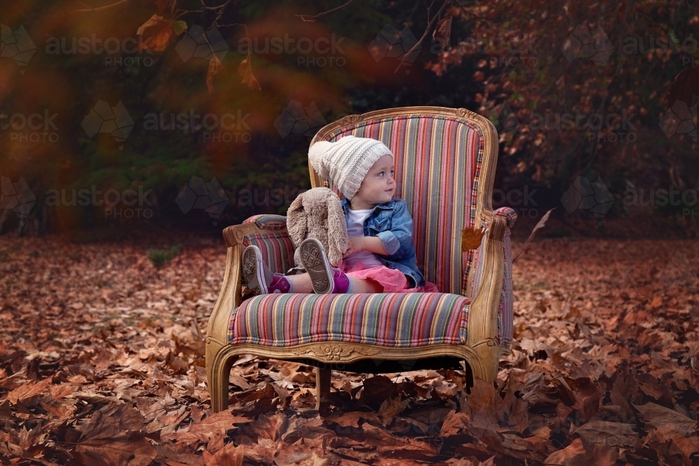 A Toddler Girl Sitting on a Chair amongst Autumn Leaves - Australian Stock Image