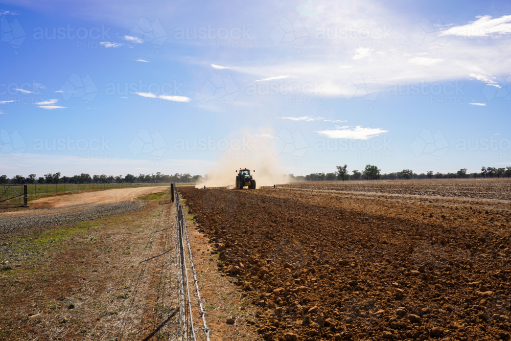 A tractor working the ground in preparation for sowing crops along a fence line - Australian Stock Image