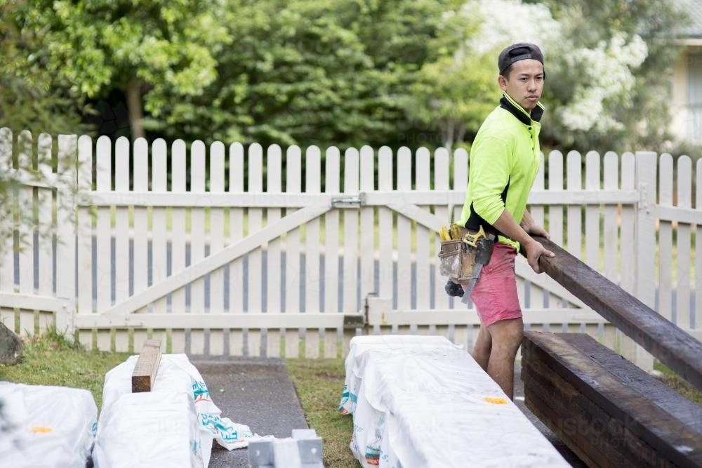 A tradesman carries a wooden beam on a home renovation site. - Australian Stock Image