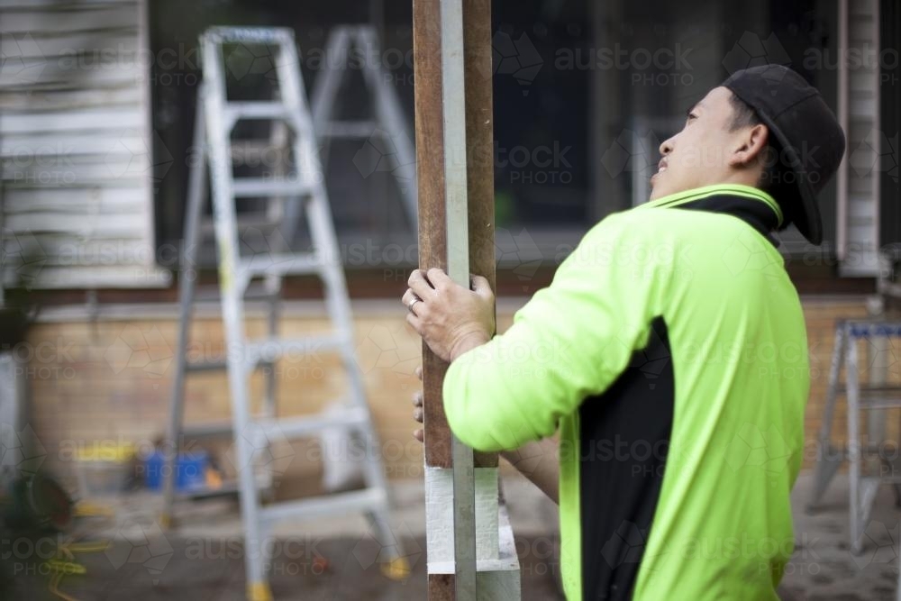 A tradesman checking the vertical axis of a wooden post. - Australian Stock Image