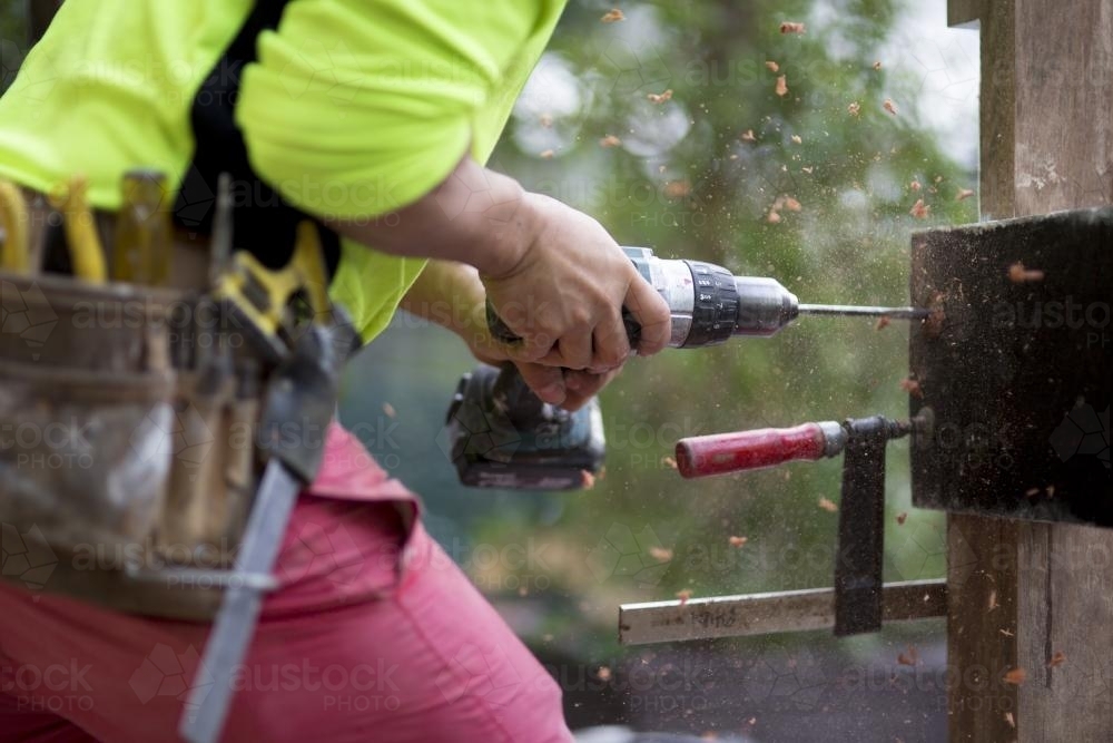 A tradesman drills into a wooden beam. - Australian Stock Image