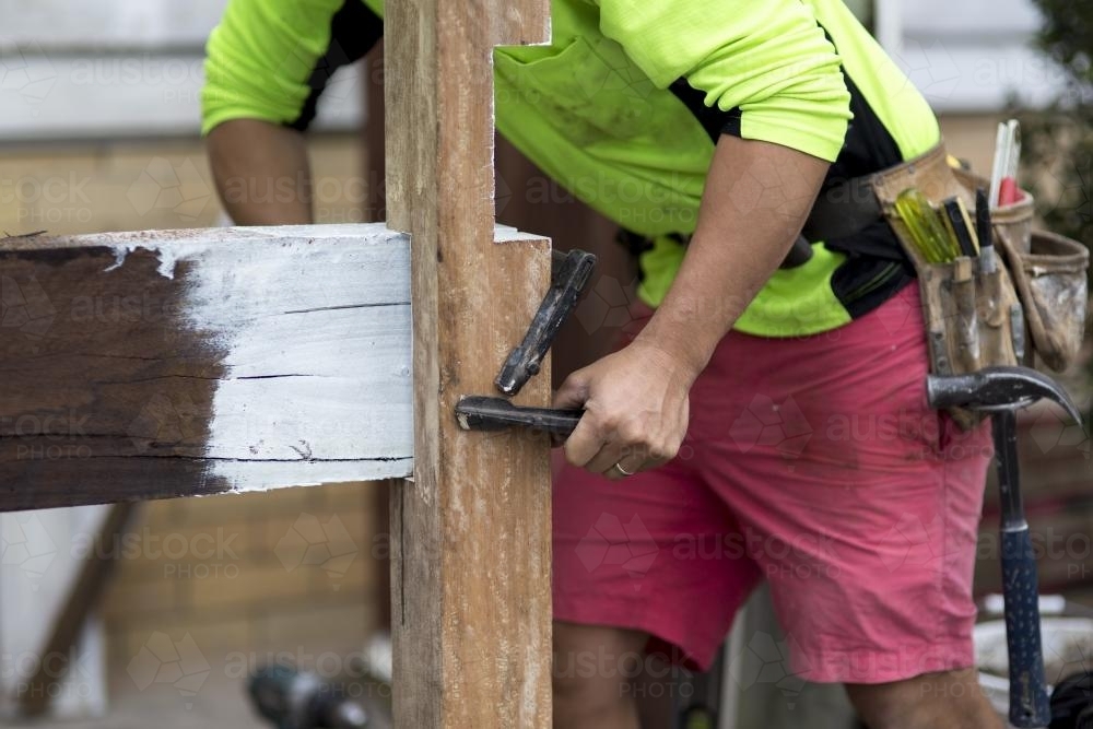 A tradesman fixing a wooden beam to a post. - Australian Stock Image