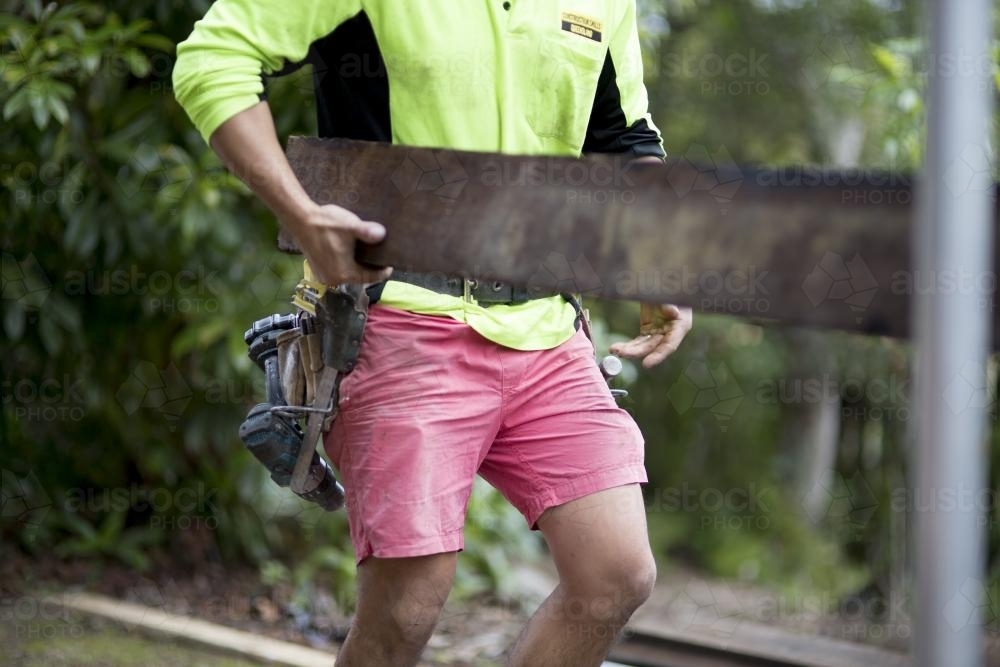 A tradesman lifts a wooden beam. - Australian Stock Image