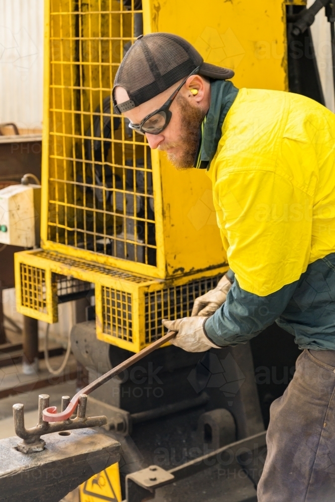A tradesman wearing high vis clothing bending steel on pegs in an anvil - Australian Stock Image
