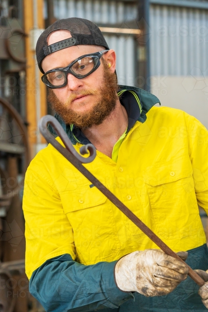 A tradesman wearing high vis clothing examining the bends in a curved steel rod - Australian Stock Image