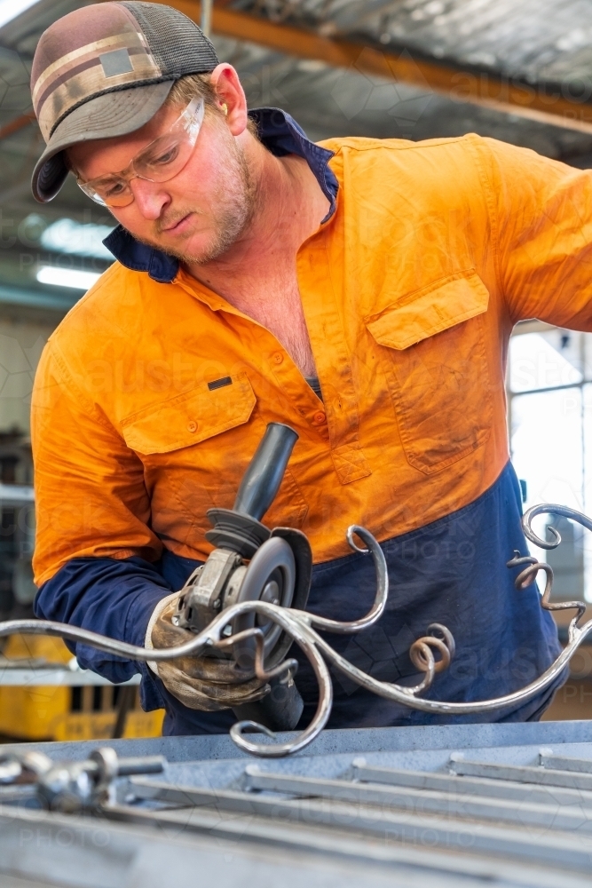 A tradesman wearing high vis clothing grinding steel on a workbench - Australian Stock Image