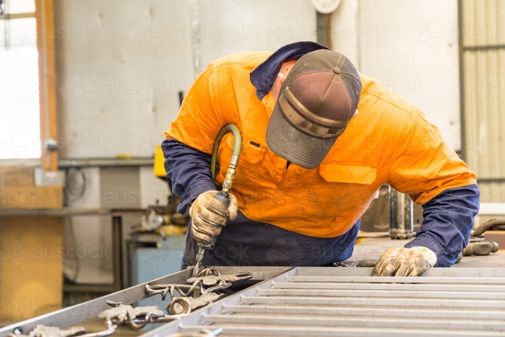 A tradesman wearing high vis clothing grinding steel on a workbench - Australian Stock Image