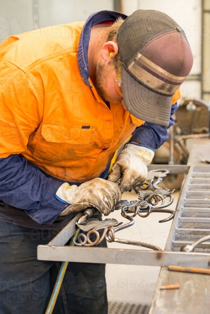 A tradesman wearing high vis clothing grinding steel on a workbench - Australian Stock Image