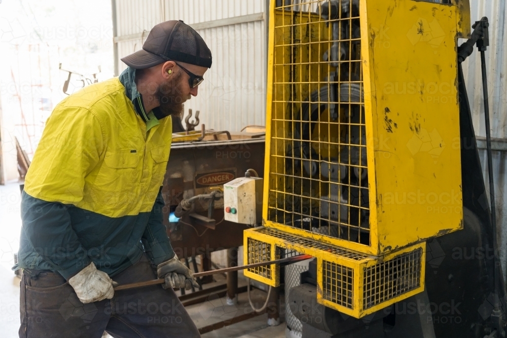 A tradesman wearing high vis clothing pushing a steel rod in a hammering machine - Australian Stock Image