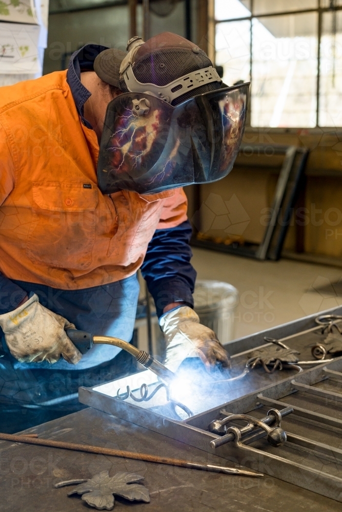 A tradesman wearing high vis clothing welding steel on a workbench - Australian Stock Image