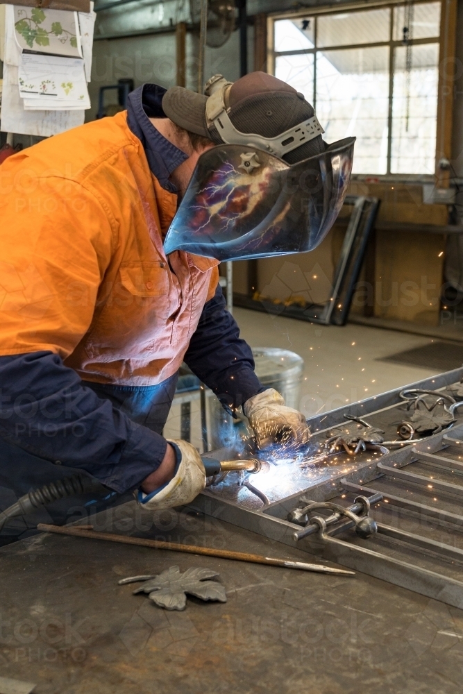 A tradesman wearing high vis clothing welding steel on a workbench - Australian Stock Image