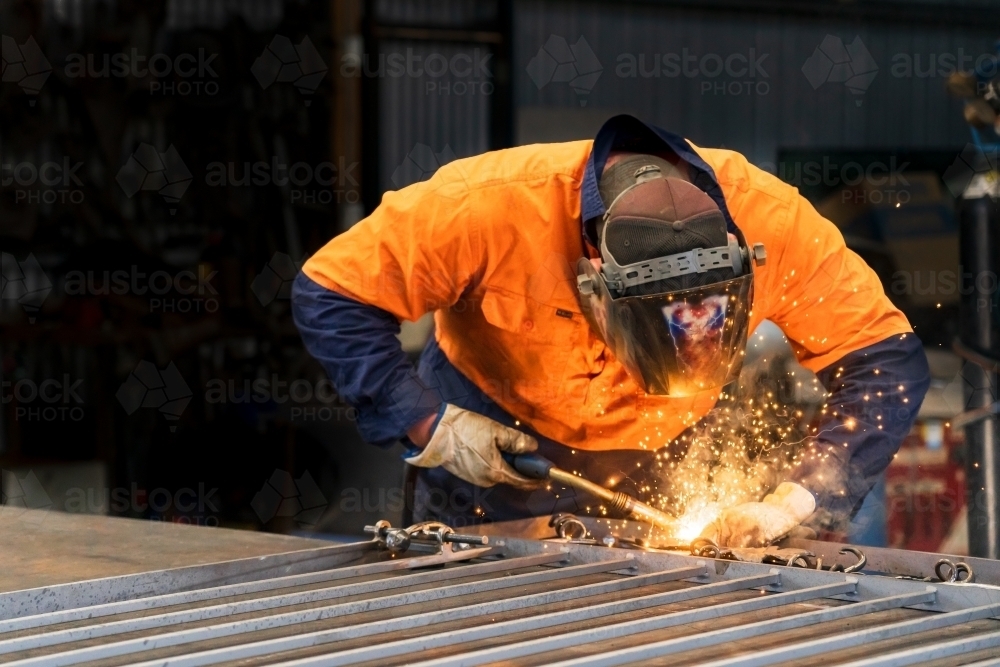 A tradesman wearing high vis clothing welding steel on a workbench - Australian Stock Image