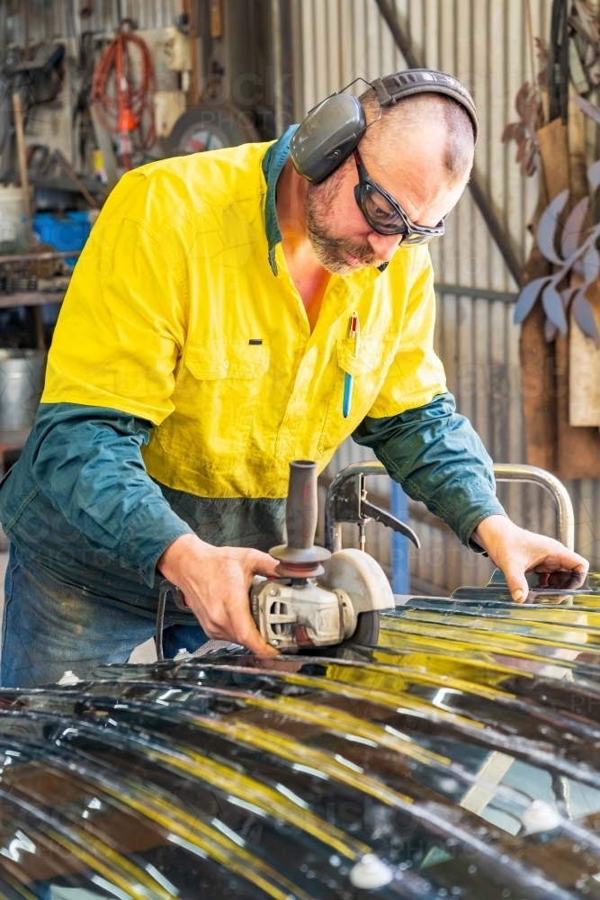 A tradesman wearing protective cutting a corrugated plastic sheet with a grinder - Australian Stock Image