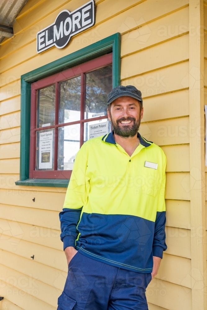 A train driver leaning on the wall of a railway station smiling - Australian Stock Image