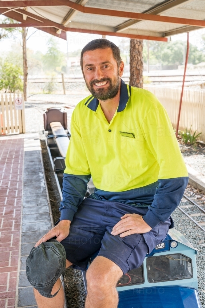 A train driver sitting on the front of a miniature railway engine smiling - Australian Stock Image