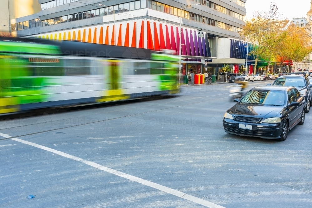 A tram rushes past cars in a busy city intersection in Melbourne - Australian Stock Image