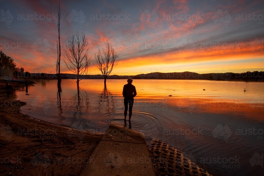A traveller watching the beautiful colourful sky and reflections on Lake Jindabyne - Australian Stock Image