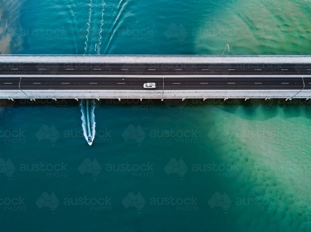 A vehicle drives over the bridge as a speed boat travels underneath leaving a wake behind - Australian Stock Image