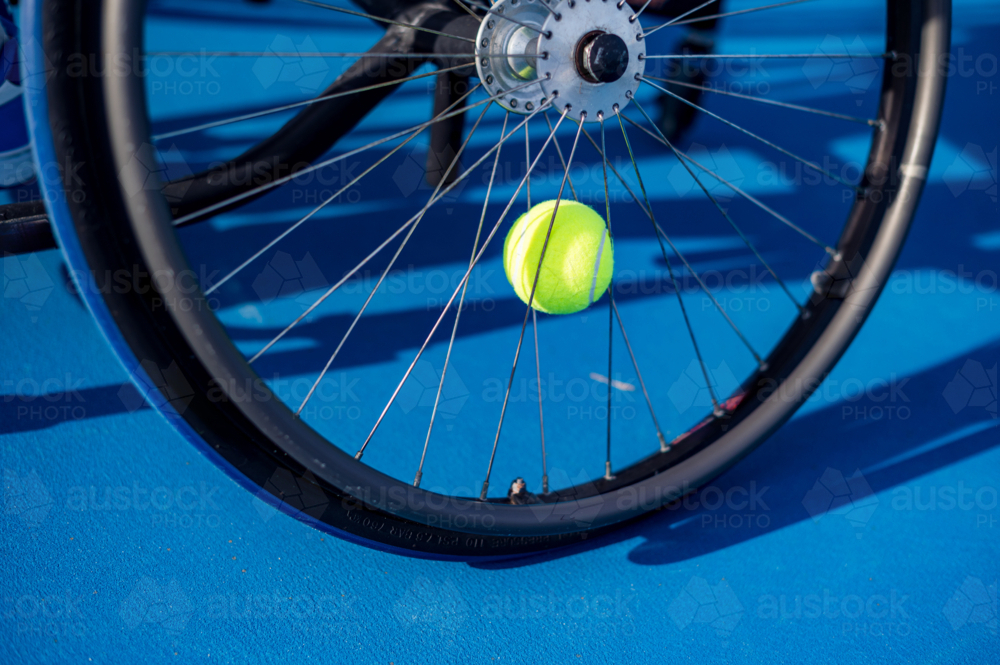 A vibrant yellow tennis ball on a wheelchair on a blue court during a match - Australian Stock Image