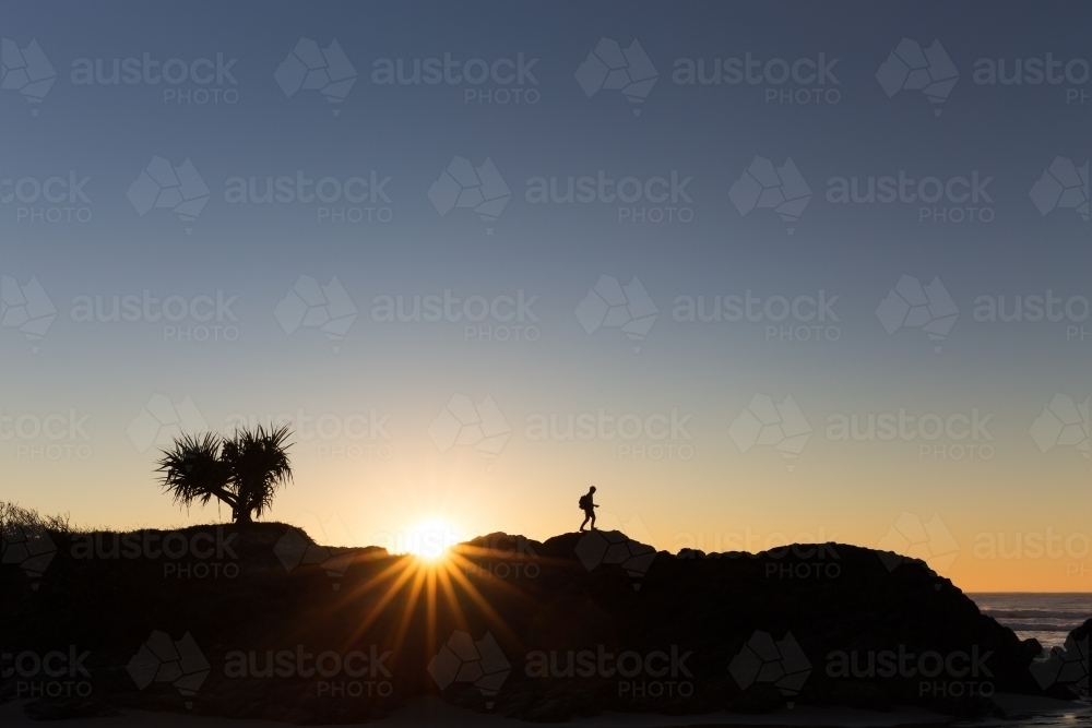 A walking hiker is silhouetted on a ridge line by a beautiful bright sunrise. - Australian Stock Image