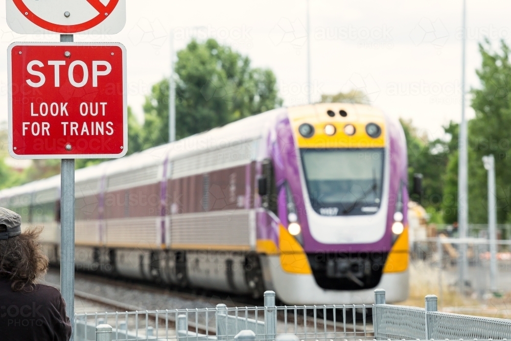 A warning sign in front of a commuter train as it approaches a pedestrian crossing - Australian Stock Image