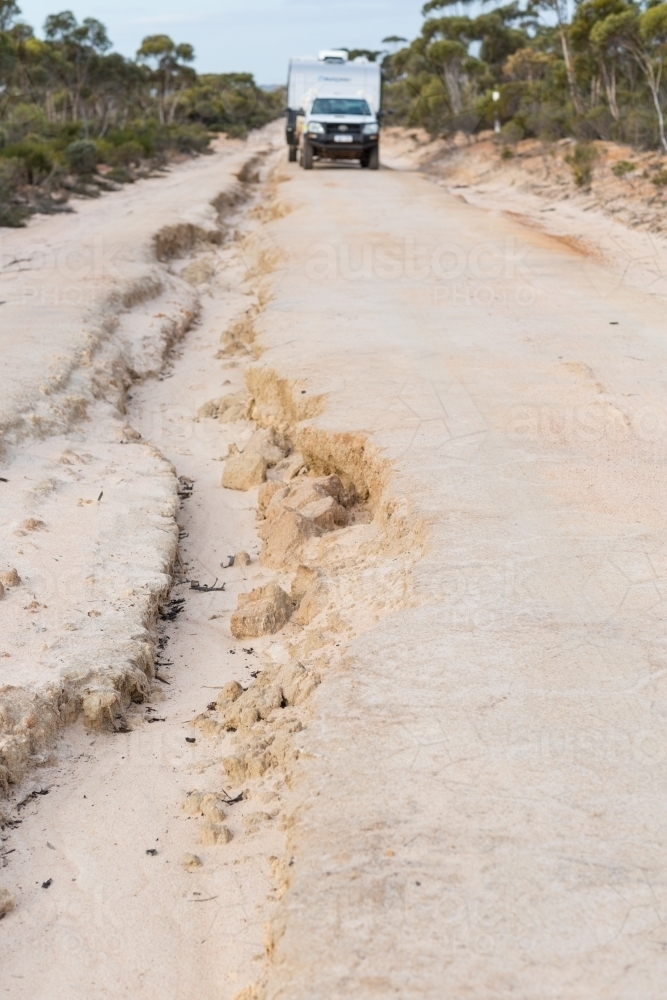 Image of A washed out unsealed road with vehicle towing a caravan