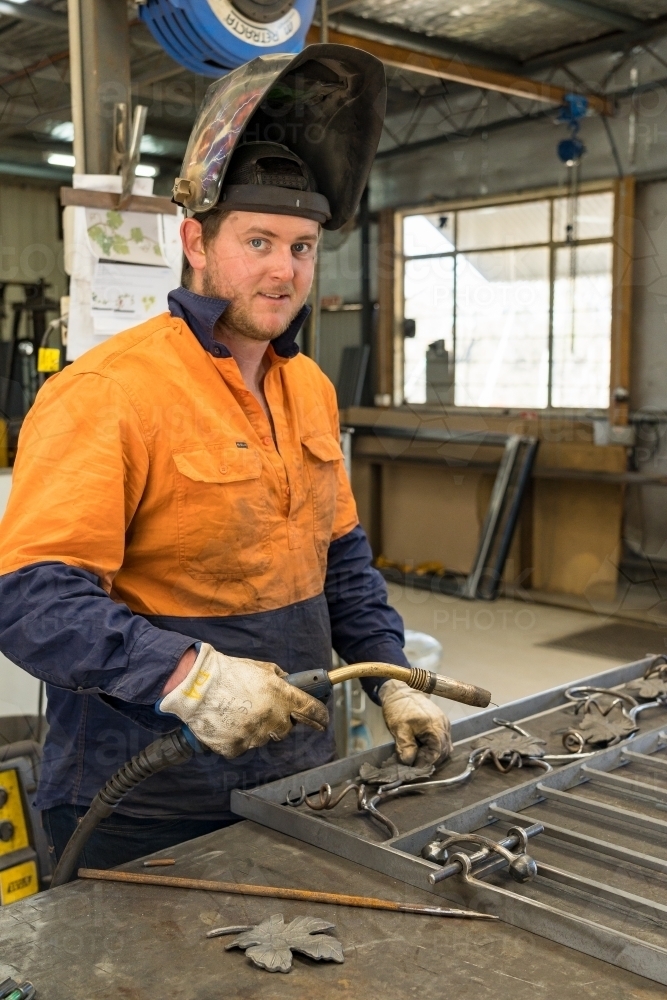 A welder with a raised visor and holding a handset smiling at the camera - Australian Stock Image