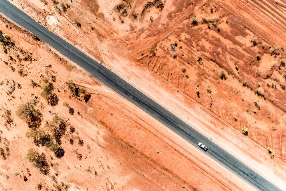 A white ute driving a rural highway straddled by red earth. - Australian Stock Image