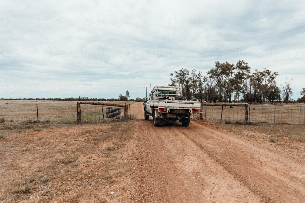 A white ute driving through gateway in farm fence. - Australian Stock Image