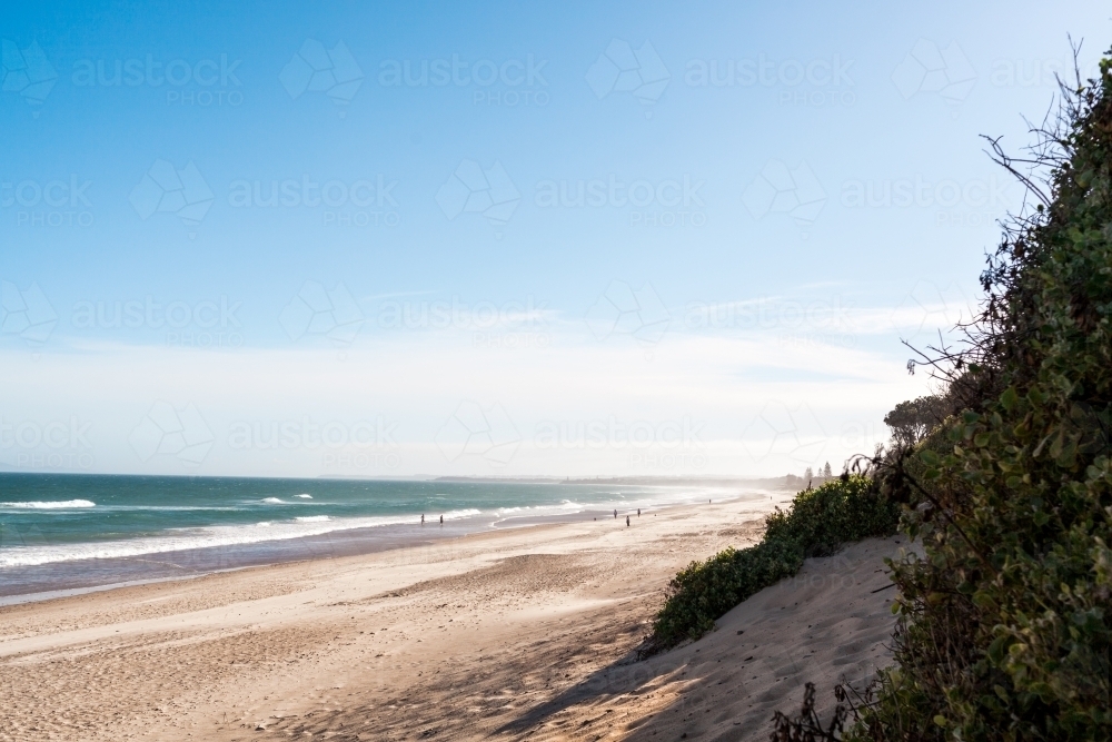 A wide outlook of people in the distance walking on a beach on a sunny afternoon - Australian Stock Image