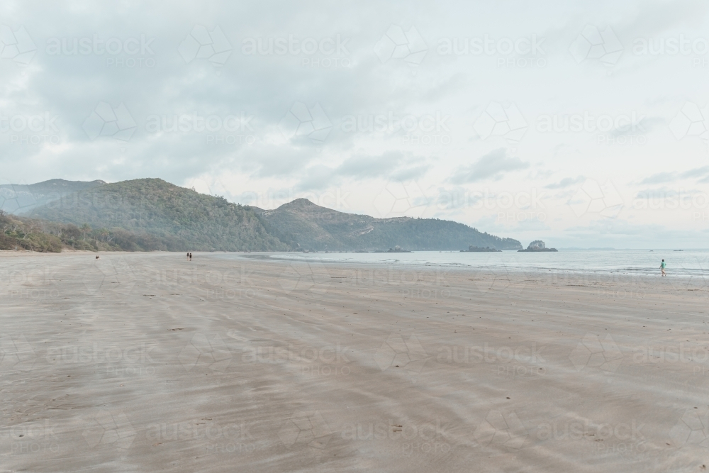 A wide, sandy beach with distant hills and mountains - Australian Stock Image