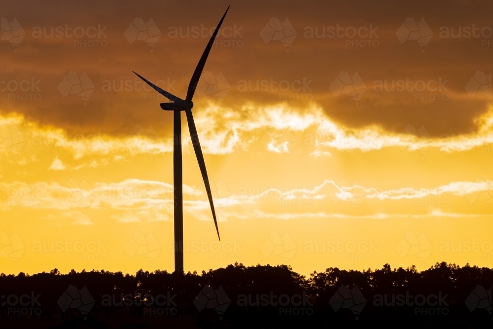 Image of A wind turbine silhouetted against a golden sunset sky ...