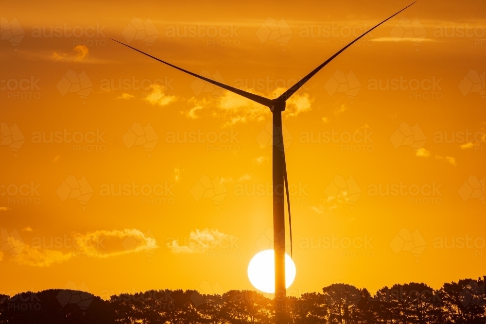 A wind turbine silhouetted against the setting sun and a golden sky - Australian Stock Image