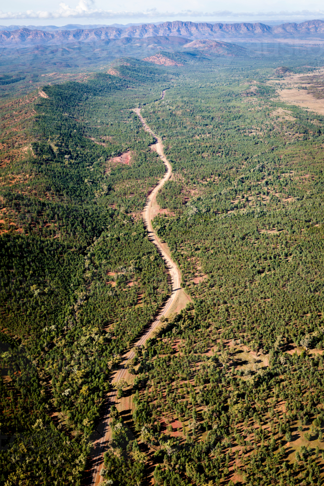 A winding dirt road through forested hills with mountain ranges beyond. - Australian Stock Image