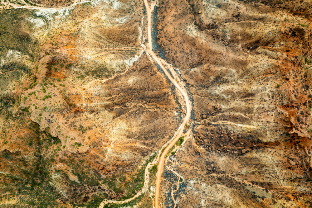 A winding outback track cutting through layered red and brown terrain. - Australian Stock Image