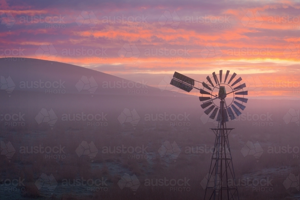 A windmill at the base of a hill in fog at sunrise - Australian Stock Image