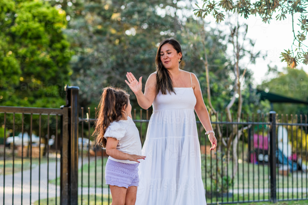 A woman and a girl stand in front a park with trees around them, enjoying their time together. - Australian Stock Image