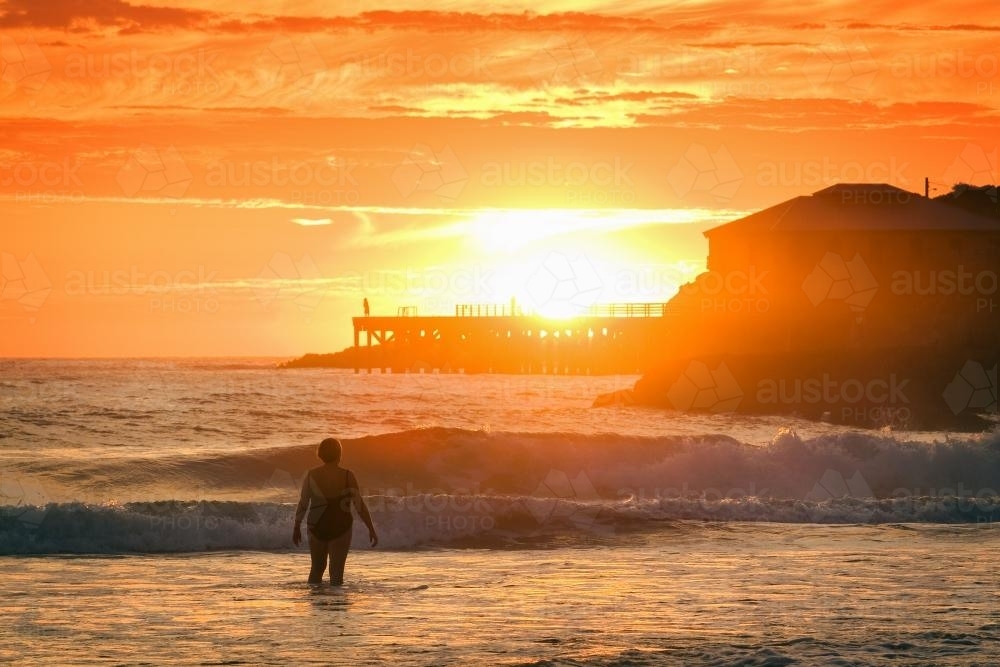 A woman at the beach at sunrise, wharf in the background. - Australian Stock Image